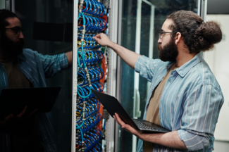 [Translate to bkw.ch: FR:] Techniker, der ein Kabel an einen Server anschließt und einen Laptop im Serverraum hält